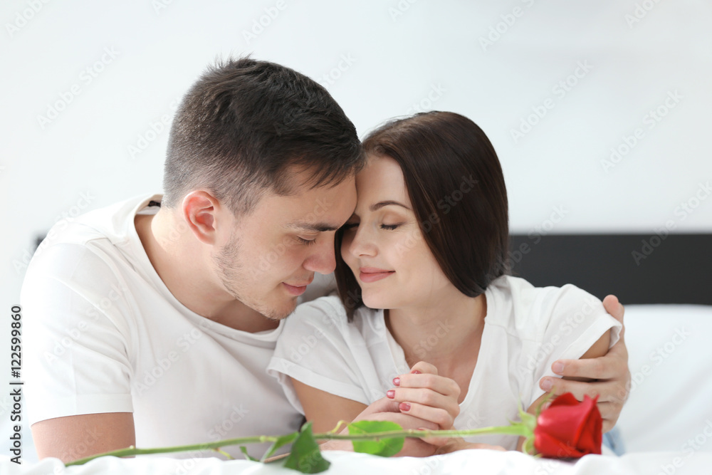 Happy couple with red rose on bed