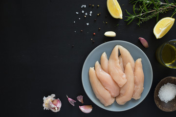 Fresh raw chicken tenders, lemon, garlic, rosemary, olive oil, pepper and salt on dark background