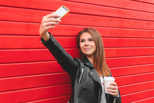 Beautiful Young Woman In A Black Leather Jacket Makes Selfie On A Red Wooden Wall