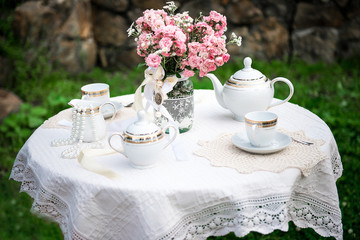 A cute table with white lace tablecloth, pink flowers in a jar, tea served for two. Picnic