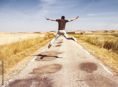 Fotografie, Obraz Chico joven saltando de alegría en una carretera vacía en medio del campo