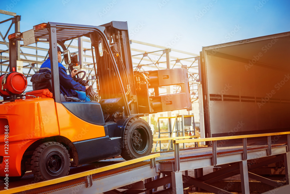 Fotografie, Obraz Forklift is putting cargo from warehouse to truck outdoors