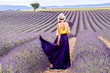 Young pretty woman in the long waving skirt and hat standing with lavender bouquet on the lavender field in Provence in France.