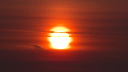 Wall Mural - Vivid red sun close up rising above cloud layers on hazy morning.