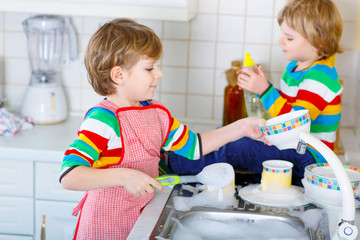 Two little kid boys washing dishes in domestic kitchen