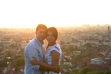 Couple Hugging On A Rooftop With An Amazing View Of The City Behind