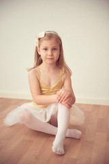 Pretty diligent ballet girl sitting in white tutu at dance studi