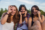Fototapeta Młodzieżowe - Girls enjoying while making silly in the park. They are making jokes and grimaces enjoying holiday. They are friends and they are imitating mustache with their hair.  