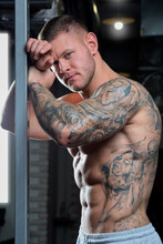 Muscular Man With Tattoos Standing In A Grey Shorts In A Gym 