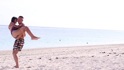 young man holds and turns his sexy girlfriend on the beach of bali island, indonesia. scene of coupl