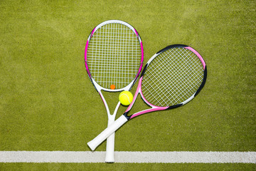 Wall Mural - Two new pink tennis rackets with a tennis ball on a green grass