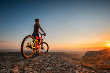 Sunset From The Top /
A Woman With A Bike Enjoys The View Of Sunset Over An Autumn Forest