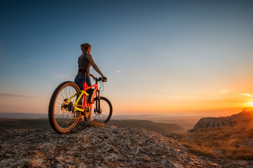 Sunset from the top /
A woman with a bike enjoys the view of sunset over an autumn forest