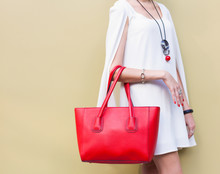 Fashionable Beautiful Big Red Handbag On The Arm Of The Girl In A Fashionable White Dress, Posing Near The Wall On A Warm Summer Night. Warm Color. Close Up