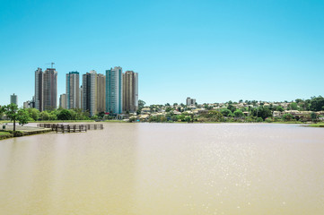 Park pond with a deck and city background and blue sky. Sunny day, landscape in a horizontal photo.