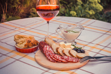 Sliced smoked sausage, home-made sausage, soft cheese, home-made bread bread on the wood plate, glass of red wine and sauce.