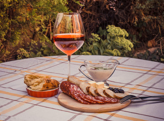 Sliced smoked sausage, home-made sausage, soft cheese, home-made bread bread on the wood plate, glass of red wine and sauce.