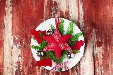 Wall Mural - Holiday decorations red star textile Christmas tree on a white plate, jingle bells, fir branches on red wooden background. Christmas background, New year.