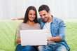 © djoronimo - Happy couple sitting on sofa at their home and using laptop.