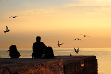 Silhouette Of Seagulls And A Girl With A Backpack On A Pier At Dawn