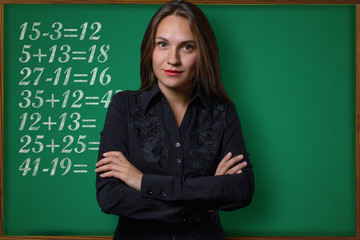 Beautiful young girl (teacher, schoolgirl, student or business woman) posing near a school blackboard with mathematical tasks