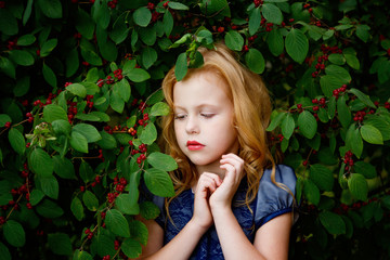 Wall Mural - Portrait of beautiful little girl in a blue dress on a background of leaves cherries