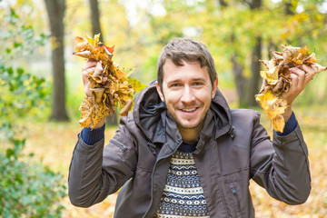 Young, cheerful man is happy in the park in autumn when leaves become colorful.