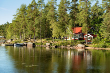 Traditional, Red Wooden House On A Lake In Småland, Sweden, In An Early Summer Morning