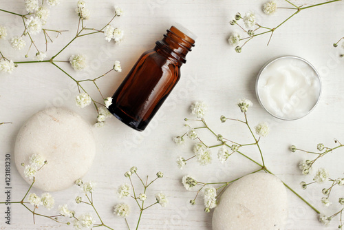 Photographie Bottle of essential oil, body care cream sample, stones, flowers