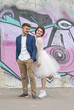 © Vladislav Plotnikov - Just married loving hipster couple in wedding dress and suit outdoor in city setting against colorful graffiti wall. Happy bride and groom walking running and dancing. Romantic Married young family.