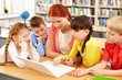 © pressmaster - A teacher sitting at table with her four students and using computer