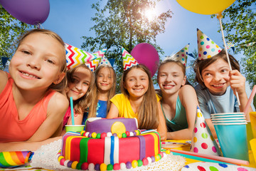 Six happy kids in party hats around birthday cake