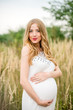 © demchyna - Portrait of a happy pregnant woman in a white dress with long blond hair in tall grass
