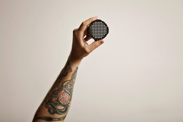 Black aeropress filter cap held up in the air by a tattooed man's hand isolated on white