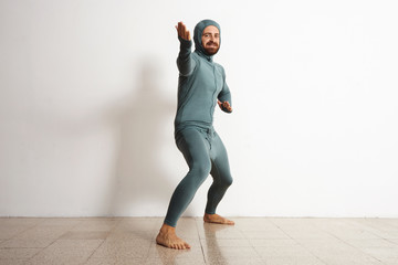 Wall Mural - Happy smiling bearded fitted male wearing snowboarding thermal baselayer suite from merino wool and acts like a ninja in welcome position, isolated on white