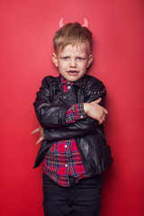 Wall Mural - Little handsome devil with horns and tail. Kid. Halloween. Studio portrait isolated over red background