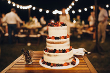 Three-level White Wedding Cake Decorated With Cream And Berries, Stands On A Table In The Banquet Area