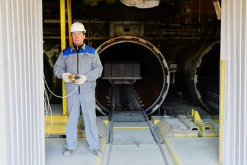 Wall Mural - Portrait of factory worker in overalls and helmet with a remote control in hand on the background of kiln brick