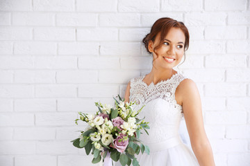 Beautiful bride with wedding bouquet on white brick wall background