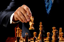 Close Up Of Man In Suit And Tie Moving Carved Wooden White Knight In Chess Game With Moody Dark Lighting