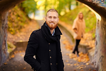 A man in a warm jacket with a female in the background.