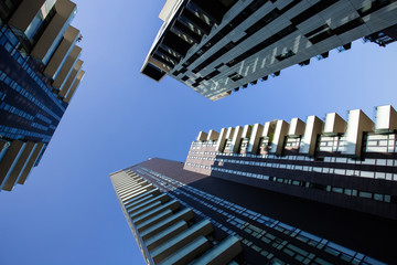 One point perspective looking straight up towards clear blue sky from ground level of tall skyscraper buildings in Milan, Italy