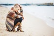 © raisondtre - Young stylish girl with short hair in a pretty cardigan and boots, is squatting on the beach in the fall and smiles. Side view.
