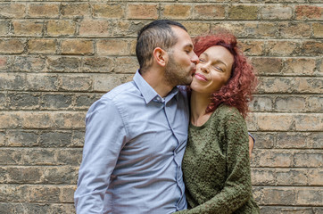 Adult couple in love in front of a brick wall enjoying the love