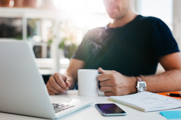 Wall Mural - Business man sitting at his desk holding a cup of coffee