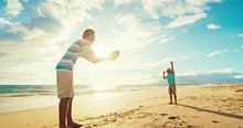 Father and son having fun on the beach at sunset, playing catch with football