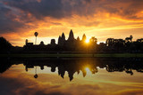 Fototapeta Krajobraz - Towers of ancient temple complex Angkor Wat at sunrise. Siem Reap, Cambodia. Temple Mountain and the sun reflected in lake at dawn. Mysterious Angkor Wat is a popular tourist attraction.
