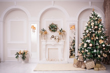 Majestic White Hall With Classical Fireplace, Arches And Mirrors. At The Wall Christmas Wreath. New Year Tree Stands In The Corner Of Room. 