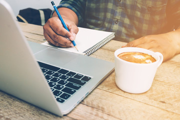 Man write on notebook with laptop and coffee cup vintage tone.