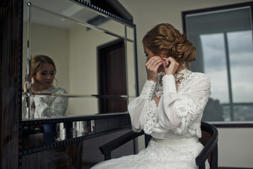 Stunning bride in old-fashioned dress adjusts her earring sittin